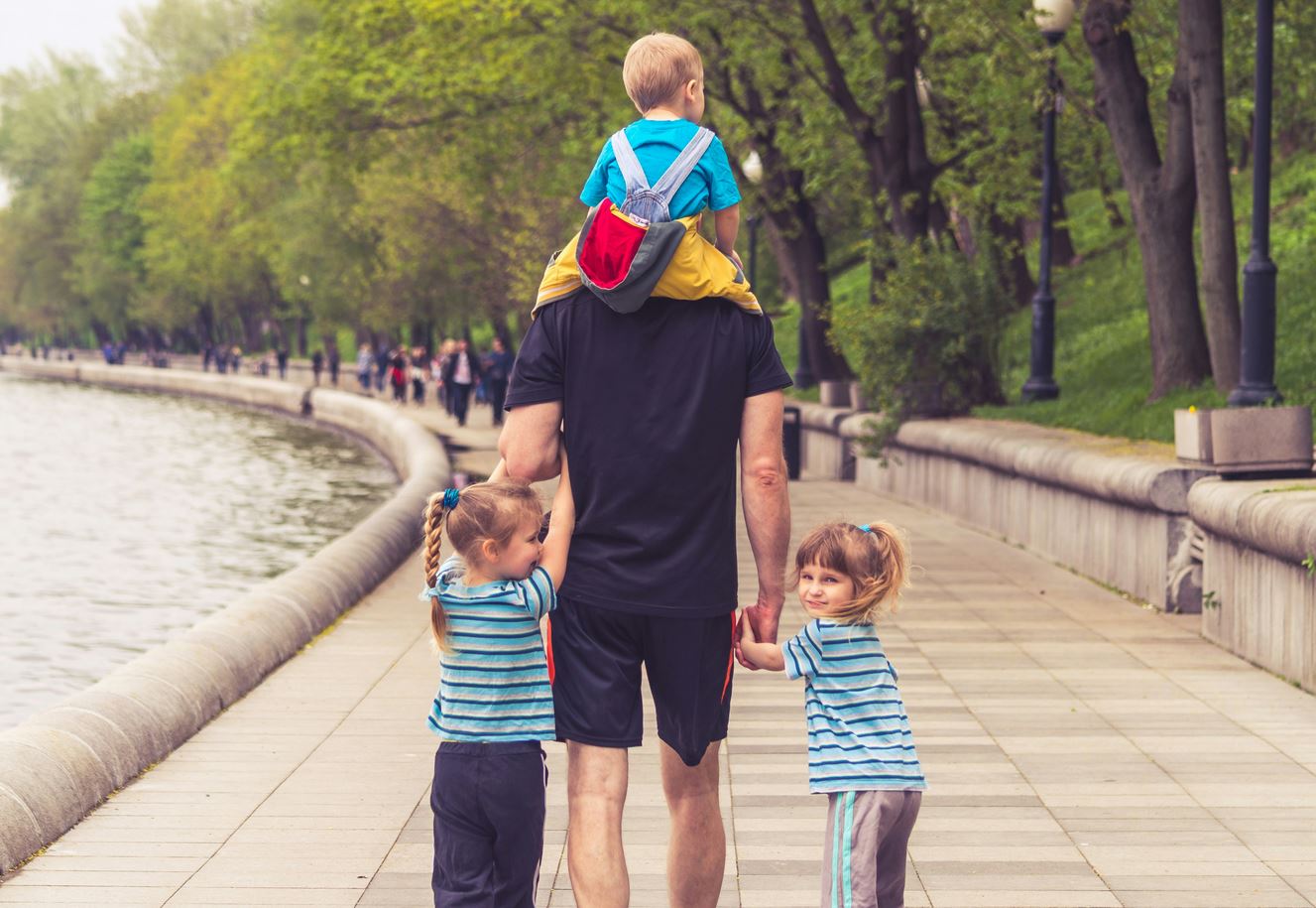 father enjoying time at park with two young daughters and young son after intense child custody battle